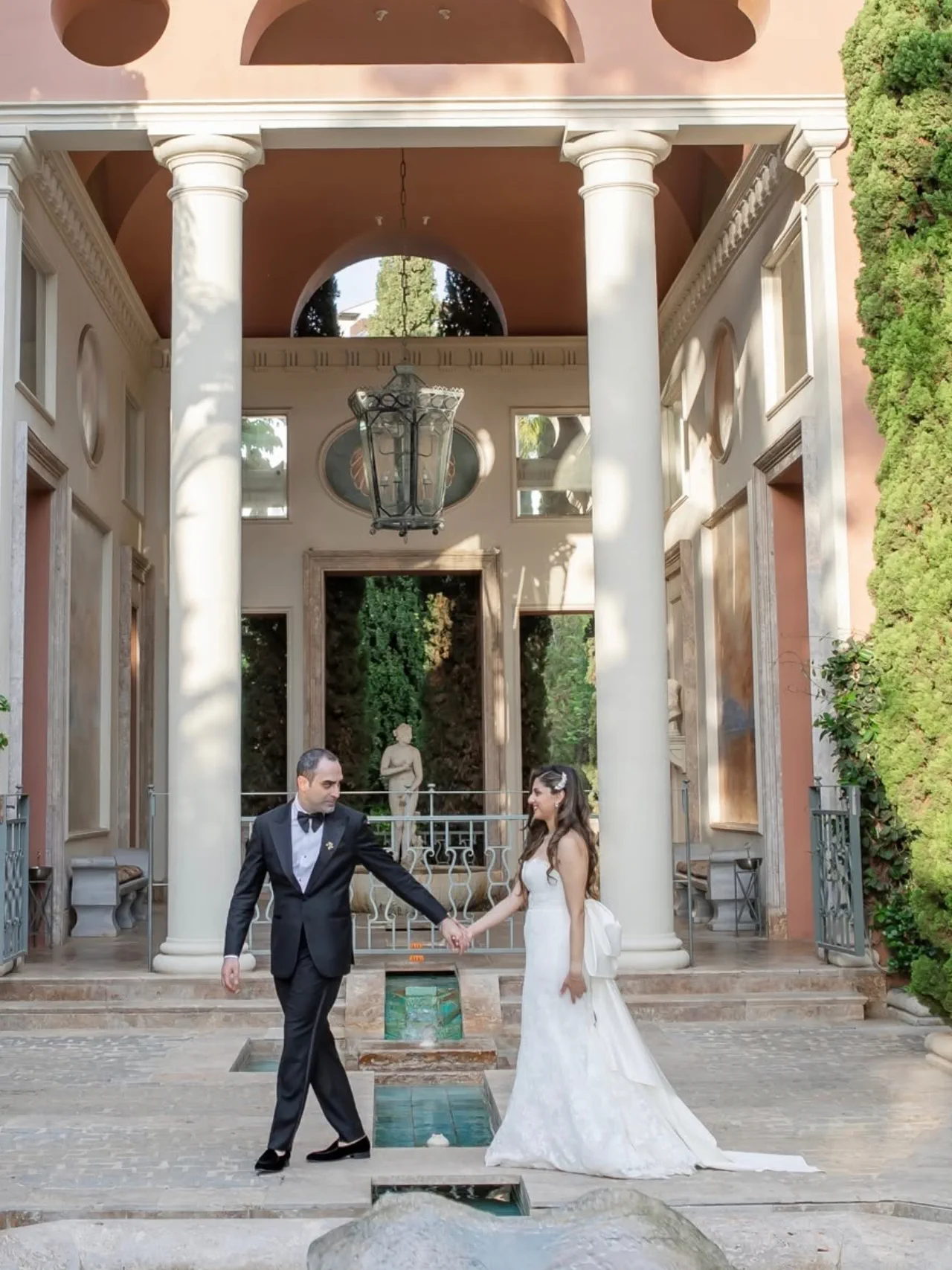 Shirin and Reza walk hand in hand beneath a colonnade at Anantara Villa Padierna