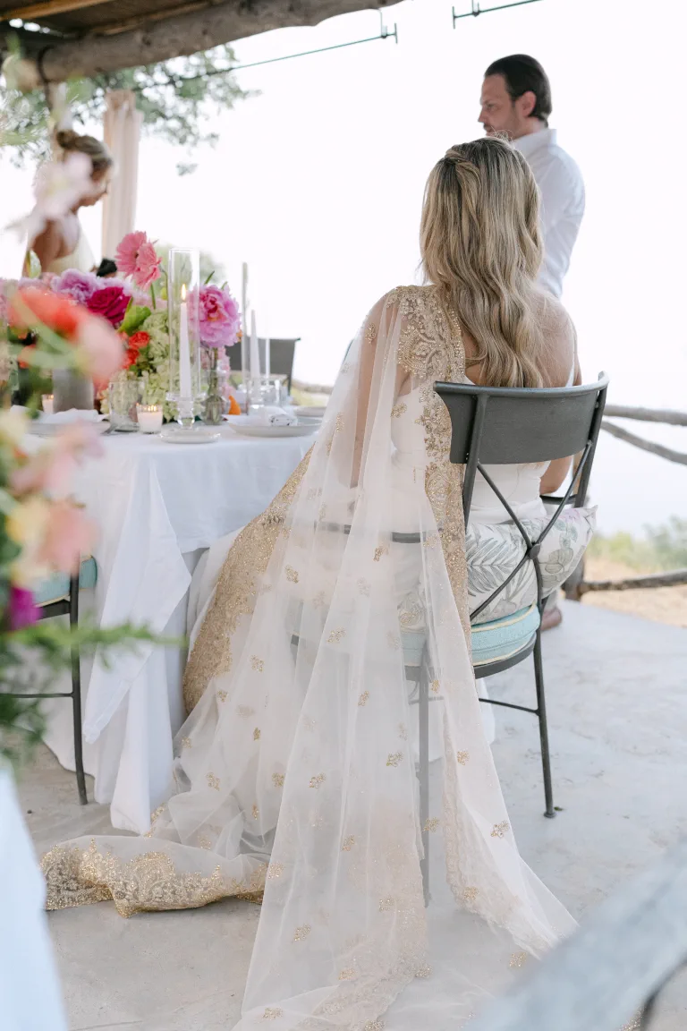 Ashton, in her embroidered cape with loose waves, by the porch table at Sa Pedrissa among flowers