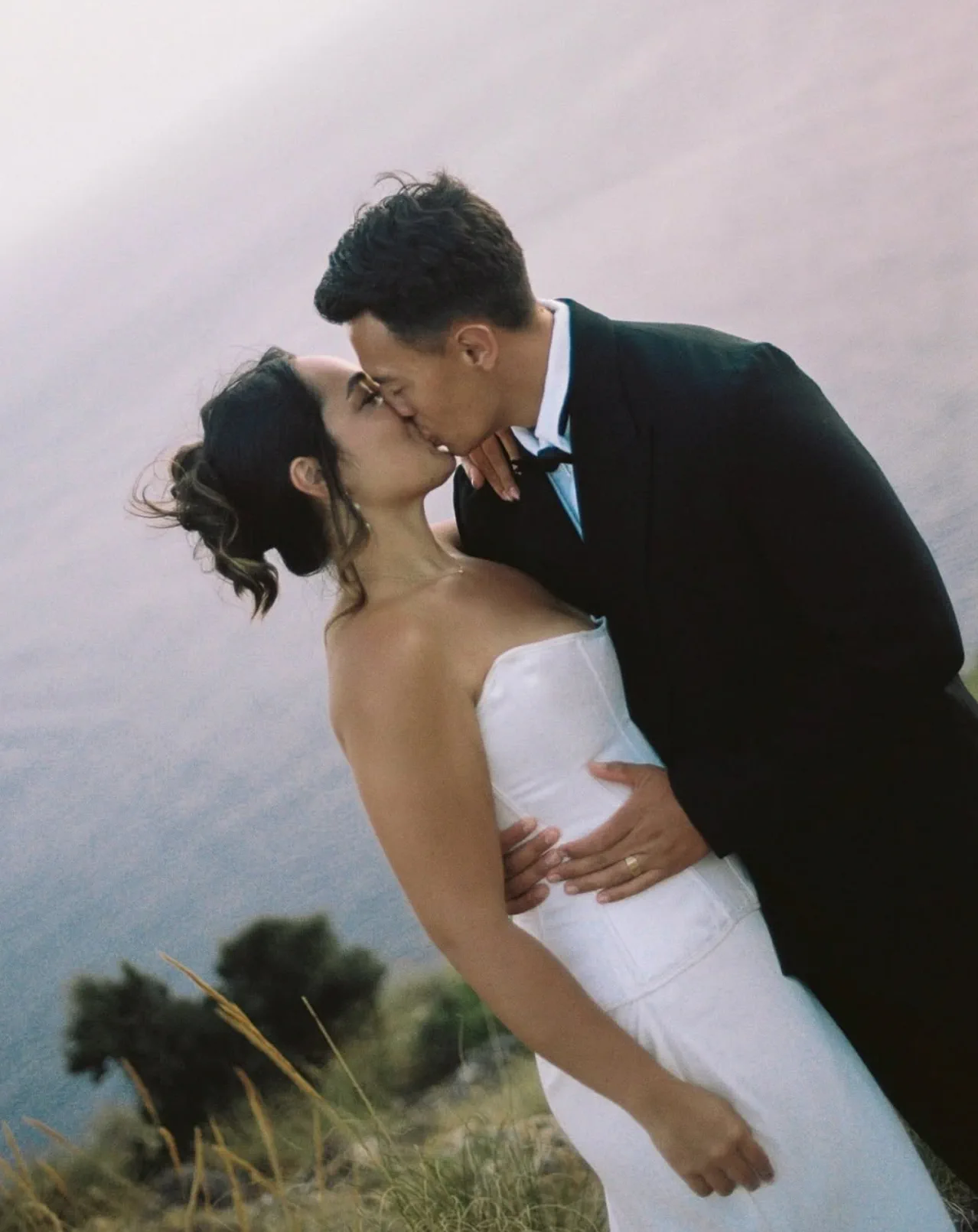 The couple kiss on the clifftop; the bride’s updo still holds its shape