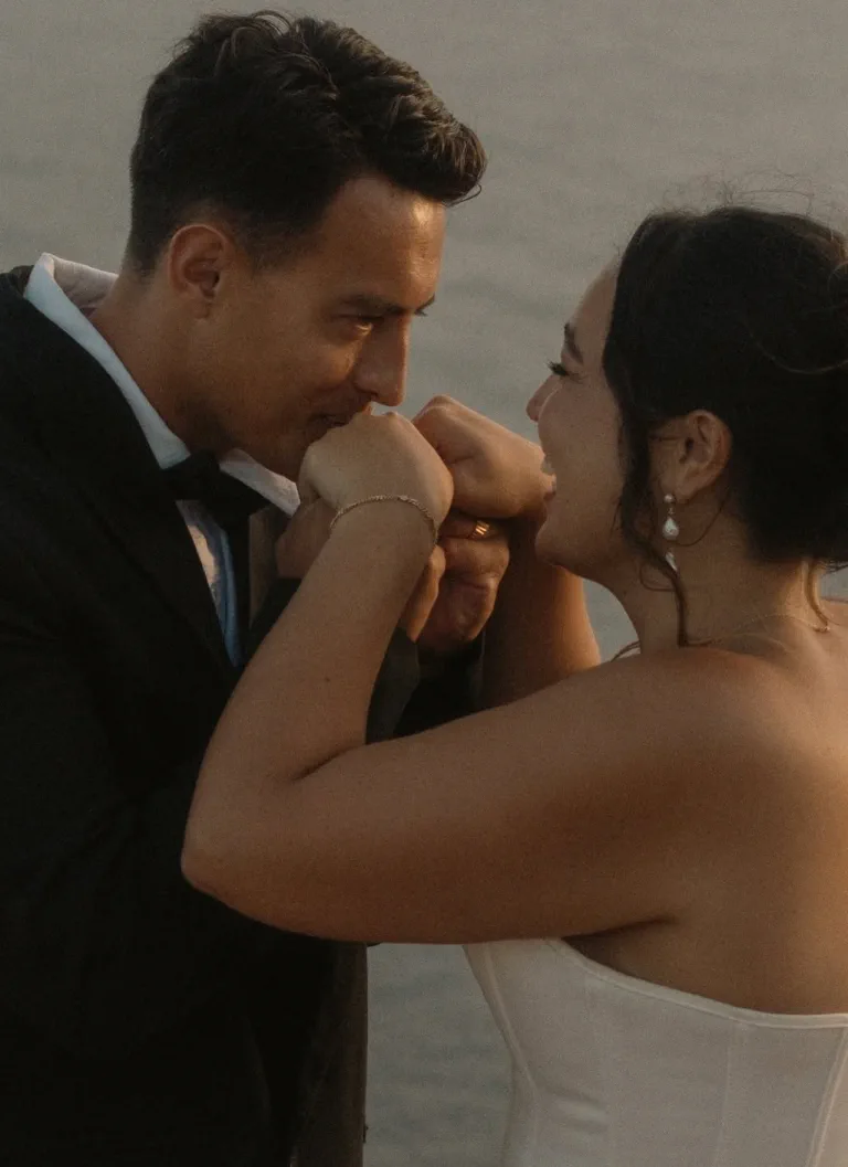 Close-up of the bride, with natural, luminous makeup and pearl earrings, as her husband kisses her hand