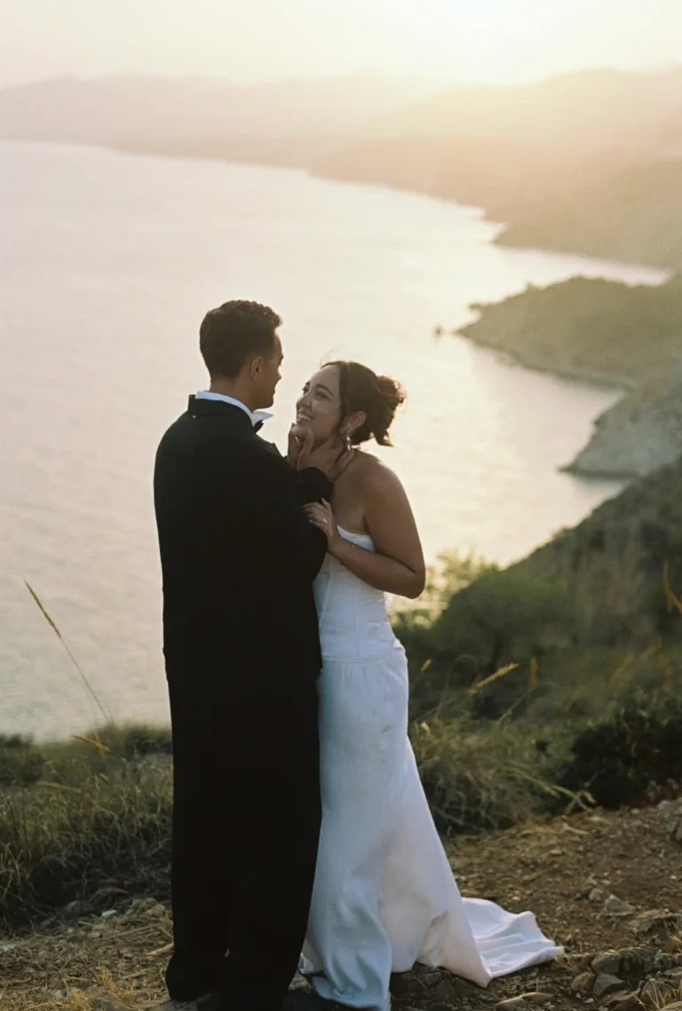 The bride smiles, her updo with loose strands, the bay at sunrise behind her