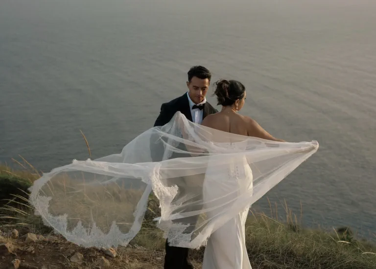 The bride holds her veil in the wind facing her husband above the sea, at an elopement in Málaga