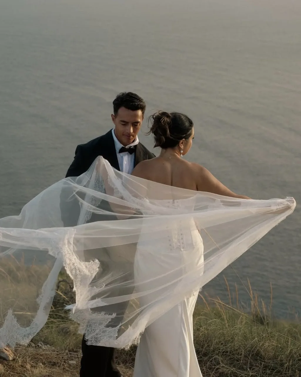 La novia sujeta el velo al viento frente a su marido sobre el mar, en una elopement en Málaga