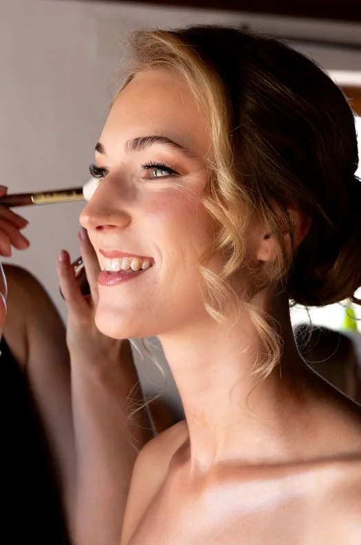 Smiling bride with warm-toned soft glam makeup and a low updo with loose strands