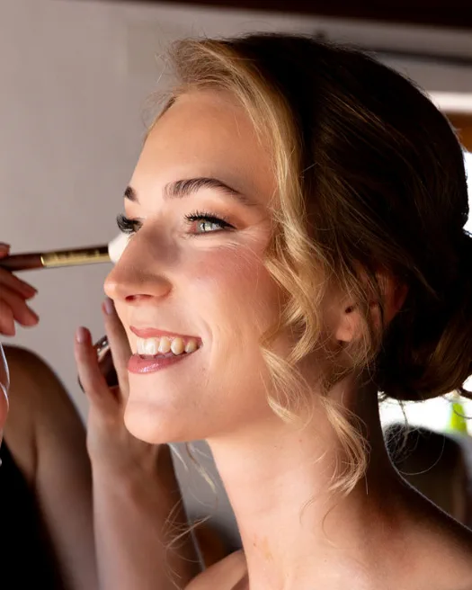 Smiling bride with warm-toned soft glam makeup as the blush goes on