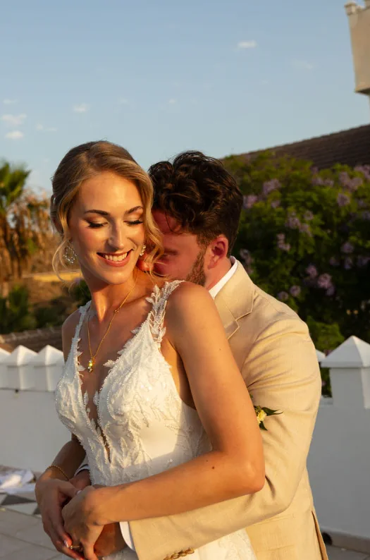 The groom holds the bride from behind at sunset on the terrace of Fort Inglés