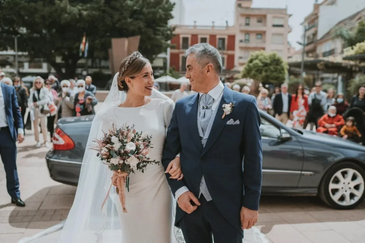 La novia, con velo largo, camina con un familiar por la plaza de la iglesia del Rosario, en Fuengirola