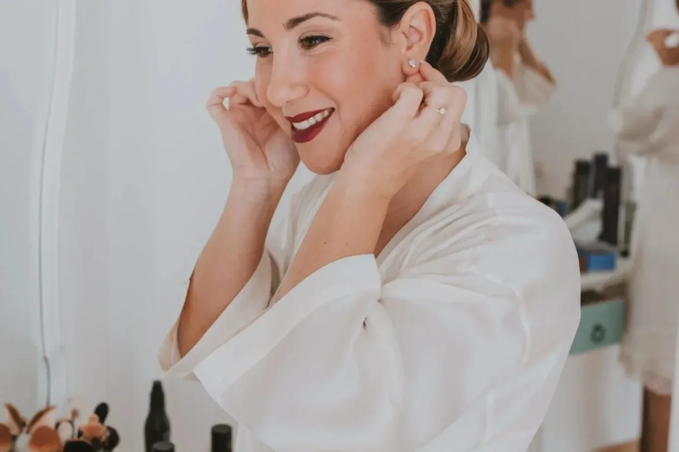 The bride puts on her earrings, her sleek updo and burgundy lips already finished