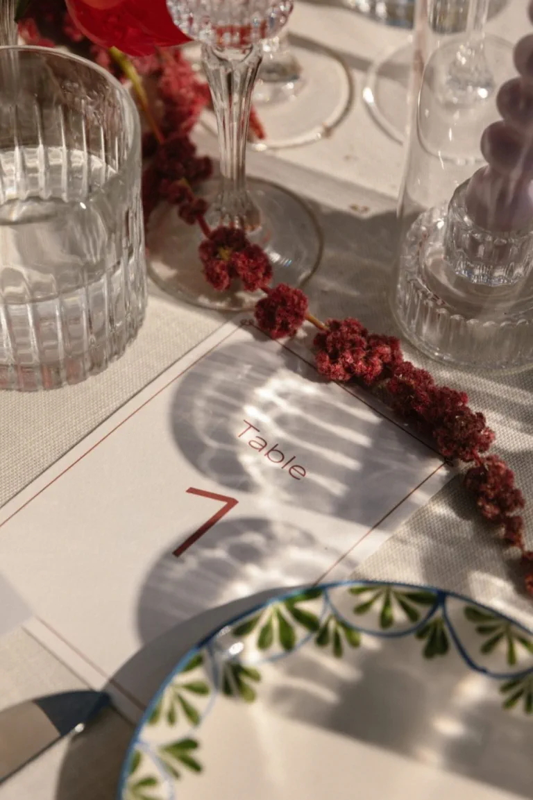 A garland of red flowers beside the glassware and the table number