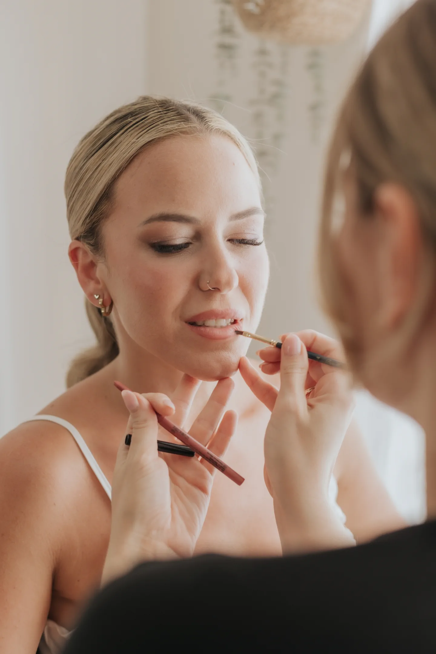 Bride with luminous soft glam makeup as the makeup artist lines her lips with a brush
