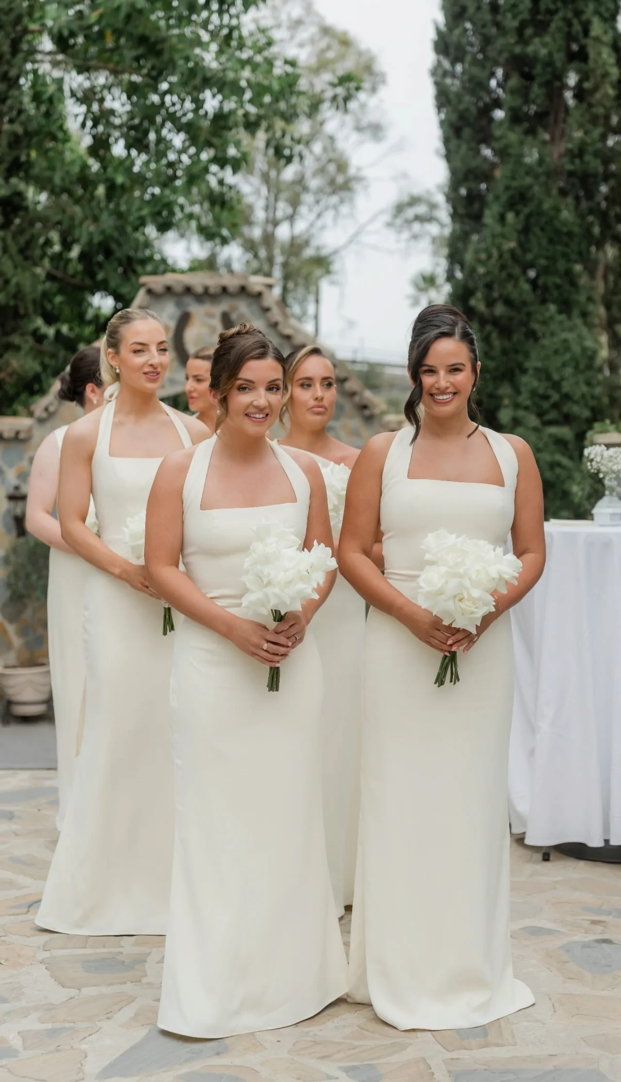 Bridesmaids in a row, in cream dresses with sleek updos and white bouquets