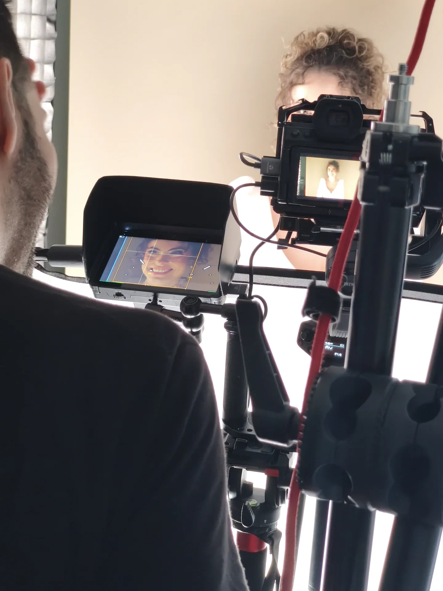 Behind the camera, the monitor shows a close-up of the model