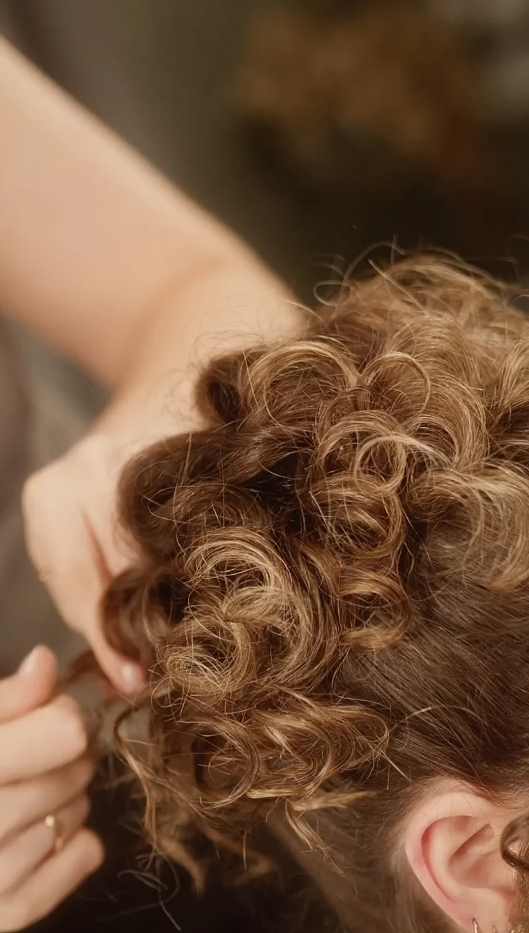 Hands placing the curls of a bridal updo while the bride gets ready